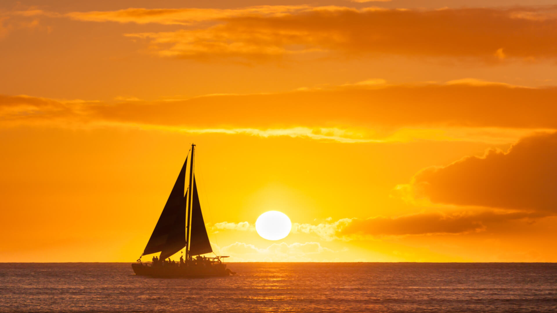 A sail boat basks in the golden glow of the sunset on an evening cruise